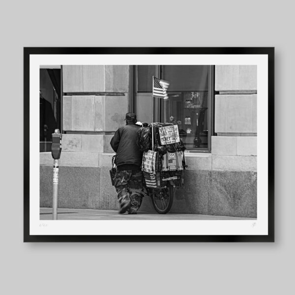 Fotografía en blanco y negro. Titulo: Going home. Veterano de guerra con su bicicleta y la bandera de USA que aún va a casa.