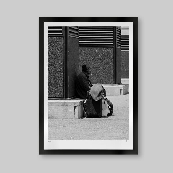 Fotografía artística en blanco y negro. Titulo: Last call home. Hombre sentado con sus maletas en la calle en espera. Atrás una columna y otras en perspectiva hacía un punto de fuga visual.