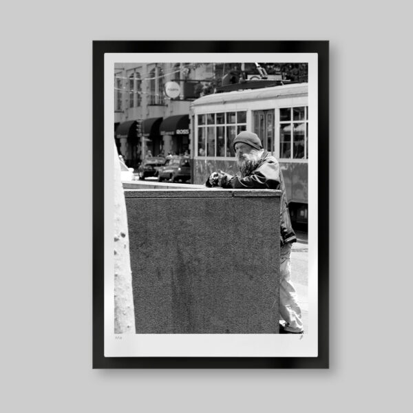 Fotografía en blanco y negro. Titulo: The traveler. Hombre con mirada reflexiva y un cigarro en la mano apoyado en un muro en la calle. Detrás el tranvía de San Francisco.