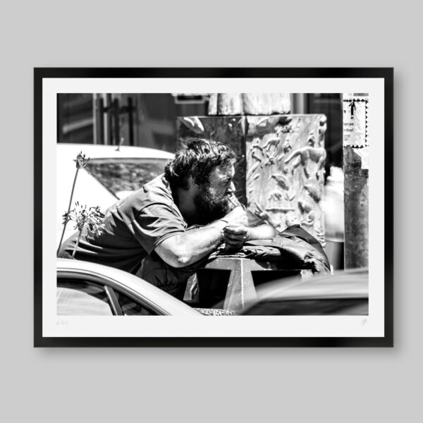 Fotografía artística en blanco y negro. Titulo: Watching the wheels. Hombre mirando los carros pasar prendiendo un cigarro.